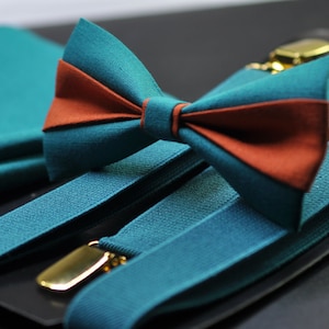 May include: Teal blue bow tie with a rust orange centre, paired with matching teal blue braces. The braces have gold metal clips.