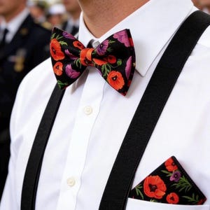 May include: A white dress shirt with a black bow tie and pocket square, both adorned with a vibrant floral pattern of red and purple poppies on a black background. Black suspenders complete the ensemble.