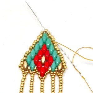 May include: Close-up of a beaded earring with a turquoise and red geometric pattern. The earring has gold beads and a fringe of gold beads.