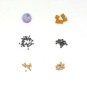 May include: Assortment of beads in various colours and sizes, including black, gold, and brown. There is also a single iridescent purple bead.