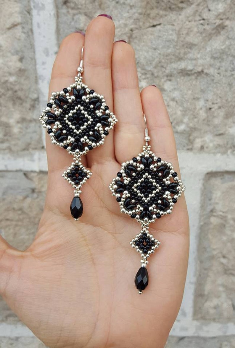 Pu&ograve; includere: Un paio di orecchini con perline nere e argentate con una perla nera a forma di lacrima che pende da ogni orecchino.