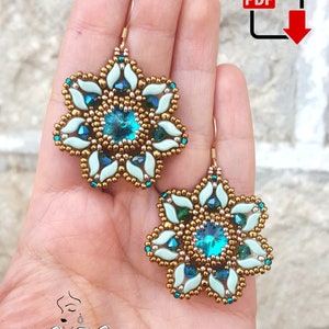 Może przedstawiać: Para złotych i turkusowych koralikowych kolczyków z kwiatowym wzorem. Kolczyki mają duży turkusowy kryształ w środku każdego kwiatu.