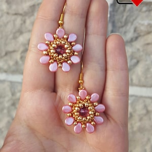 May include: A pair of pink and gold beaded flower earrings. The earrings are made with small pink and gold beads and have a gold hook.