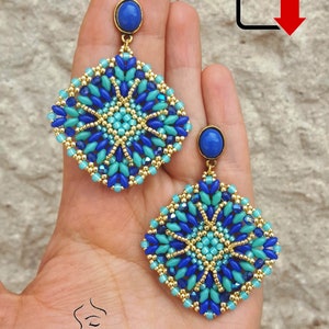 Pode incluir: Um par de brincos quadrados de contas azuis e douradas com uma pedra preciosa azul no topo. Os brincos são feitos à mão e têm um design geométrico.