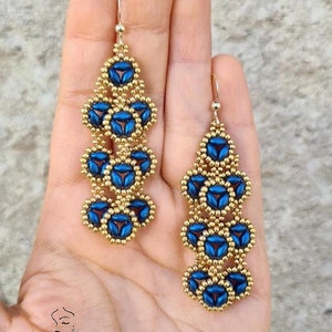 Puede incluir: Un par de pendientes largos y colgantes con un diseño dorado y azul. Los pendientes están hechos de pequeñas cuentas y tienen un patrón en cascada.