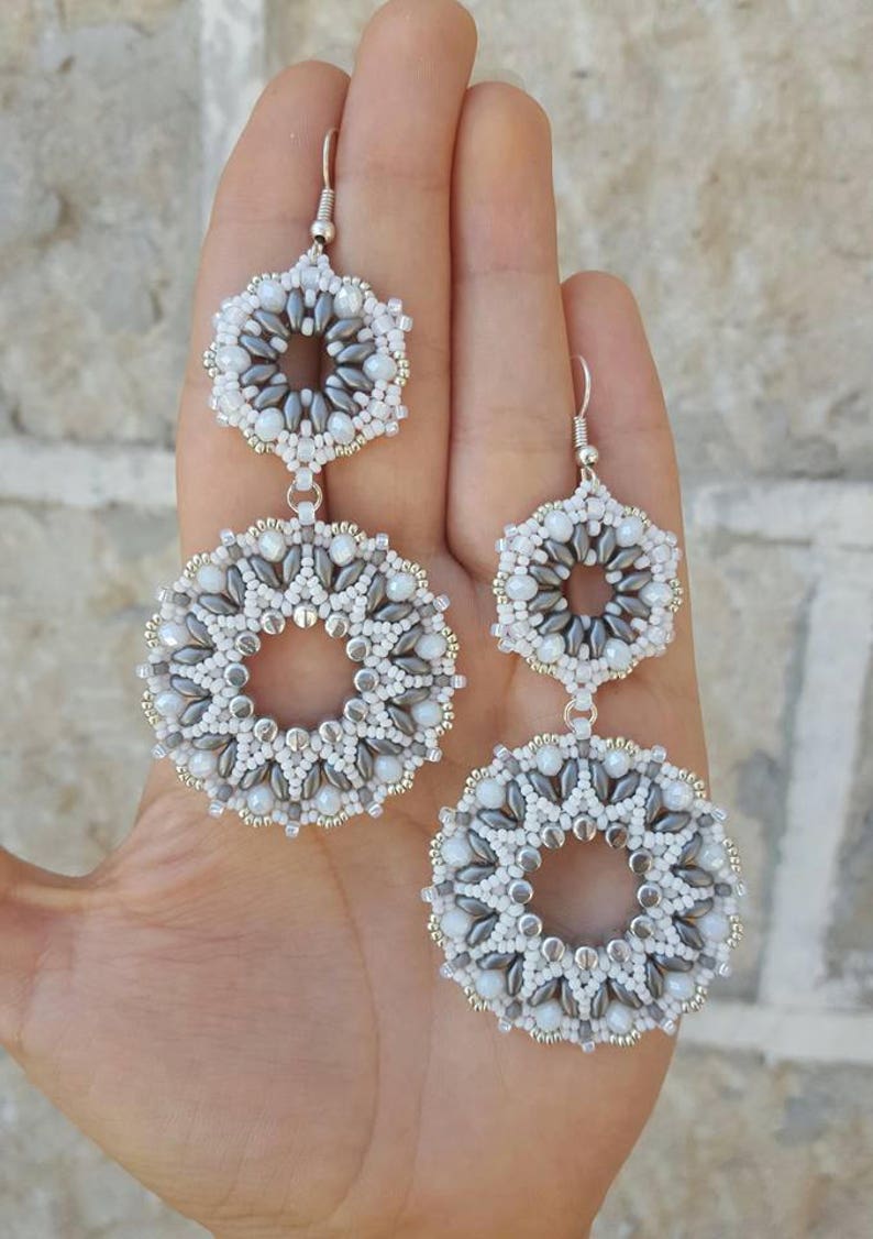 May include: A pair of silver dangle earrings with two beaded circles, one larger than the other. The circles are made of white and gray beads.