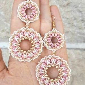 May include: A pair of pink and gold beaded earrings with a circular design. The earrings are made with small beads and have a delicate, feminine look.