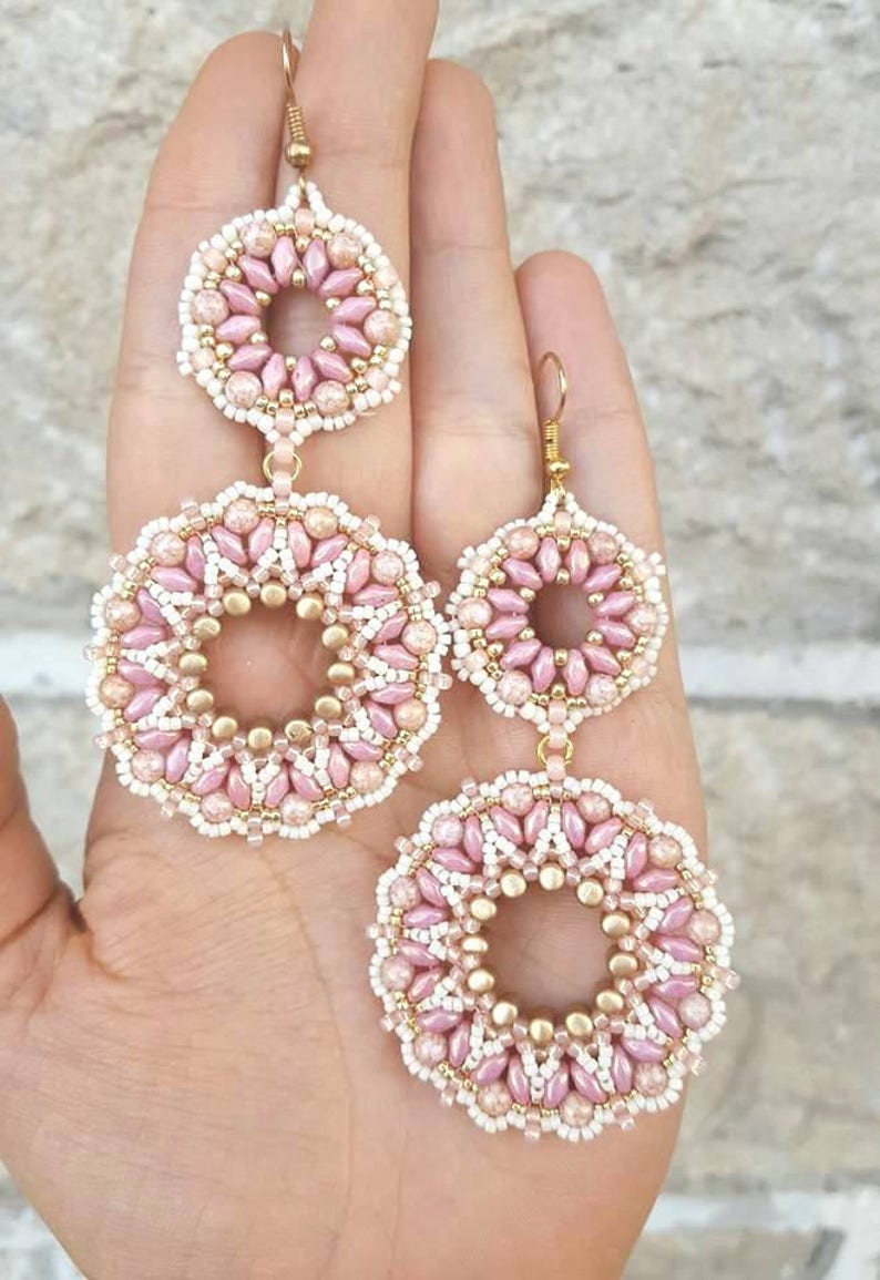 May include: A pair of pink and gold beaded earrings with a circular design. The earrings are made with small beads and have a delicate, feminine look.