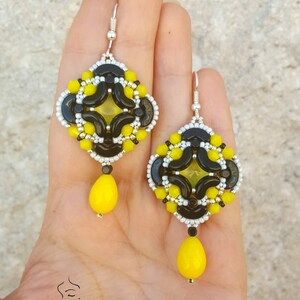May include: A pair of black and yellow beaded earrings with a teardrop-shaped yellow bead dangling from each earring.
