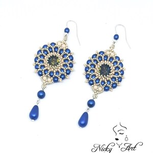 Peut inclure: Une paire de boucles d'oreilles en perles bleues et cr&egrave;me avec un pendentif en forme de larme. Les boucles d'oreilles pr&eacute;sentent un motif rond en perles avec une petite pierre iris&eacute;e au centre.