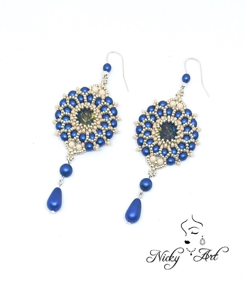 Peut inclure: Une paire de boucles d'oreilles en perles bleues et cr&egrave;me avec un pendentif en forme de larme. Les boucles d'oreilles pr&eacute;sentent un motif rond en perles avec une petite pierre iris&eacute;e au centre.