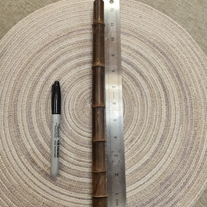 May include: A dark brown bamboo stick with a cylindrical shape, approximately 11 inches long, is displayed next to a silver ruler and a black Sharpie marker. The bamboo has visible nodes and a natural wood grain.