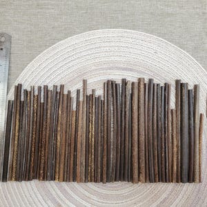 May include: A collection of various-sized, brown wooden sticks arranged on a woven placemat. A metal ruler with inch markings and a black Sharpie marker are also present. The sticks vary in color and texture.