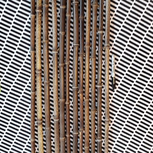 May include: A collection of 14 brown bamboo sticks of varying lengths, arranged vertically on a black and white checkered surface.