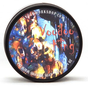May include: A round black container of shaving soap with a textured lid edge. The label features a colorful, abstract illustration with the text Voodoo King, CAYUENWORKSHOP.COM, and PREMIUM SHAVING SOAP NET WT. 4 OZ printed in white and red.