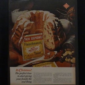 May include: A vintage advertisement for Fleischmann's Yeast, featuring a glazed bundt cake with a red and white design. The text reads "It's Christmas! The perfect time to start giving your family the real thing."  The ad also includes a packet of Fleischmann's Yeast with the text "New Rapidmix Fleischmann's New Improved Active Dry Yeast Net Wt. 1/4 oz."