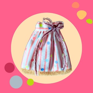 Può includere: Una gonna a righe rosa e bianche con pois colorati e un nastro viola. La gonna ha un bordo in pizzo ed è realizzata in un tessuto morbido e testurizzato.