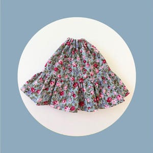Può includere: Gonna con stampa floreale nei toni del blu, rosa e verde. La gonna presenta un orlo a balze e una vita elasticizzata. Il tessuto è ricoperto da un motivo di rose e altri fiori.