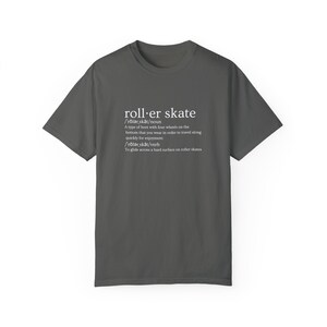 May include: A dark gray t-shirt with a white graphic design that defines the word "roller skate" as a type of boot with four wheels and a verb meaning to glide across a hard surface on roller skates.