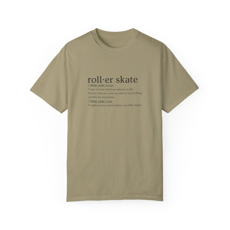 May include: A khaki t-shirt with a black graphic print of the word "roller skate" defined as a type of boot with four wheels on the bottom that you wear to travel quickly for enjoyment. The definition also includes the verb "roller skate" defined as to glide across a hard surface on roller skates.