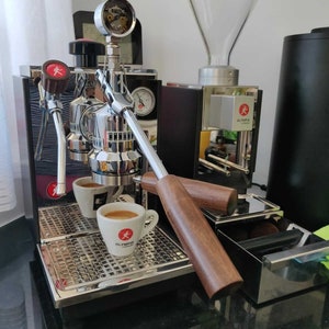 May include: A silver espresso machine with two cups of espresso on a drip tray. The machine has a wooden handle and a pressure gauge. The machine is labeled "OLYMPIA EXPRESS".