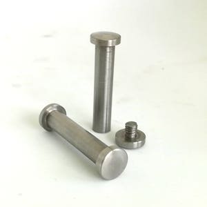May include: Two silver metal bolts with rounded heads and threaded ends. The bolts are lying on a white surface.