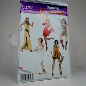 May include: A Simplicity Costumes sewing pattern envelope S0793 featuring illustrations of five different historical and fantasy outfits, including an Egyptian gown, a flapper dress, a leopard print tunic, a white toga, and a fringed hunter costume.