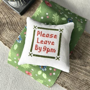 The finished pillow, made from this cross stitch pattern, is sitting on a board.