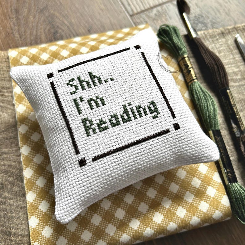 The finished pillow, made from this cross stitch pattern, is sitting on a wooden board.