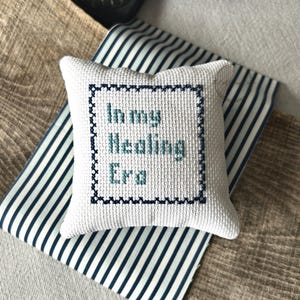 The finished pillow, made from this cross stitch pattern, is sitting on a wooden board.