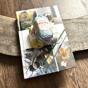 The yarn, used in this crochet pattern, is sitting on a book with crochet hooks.