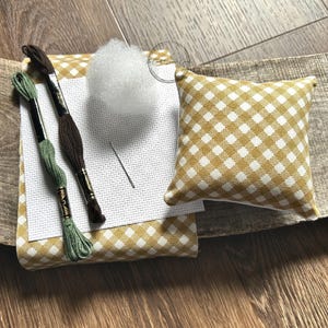 The supplies needed to make this cross stitch mini pillow are sitting on a wooden board.
