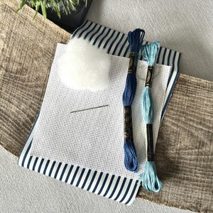 The supplies needed to make this cross stitch mini pillow are sitting on a wooden board.