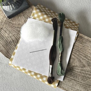 The supplies needed to make this cross stitch mini pillow are sitting on a wooden board.