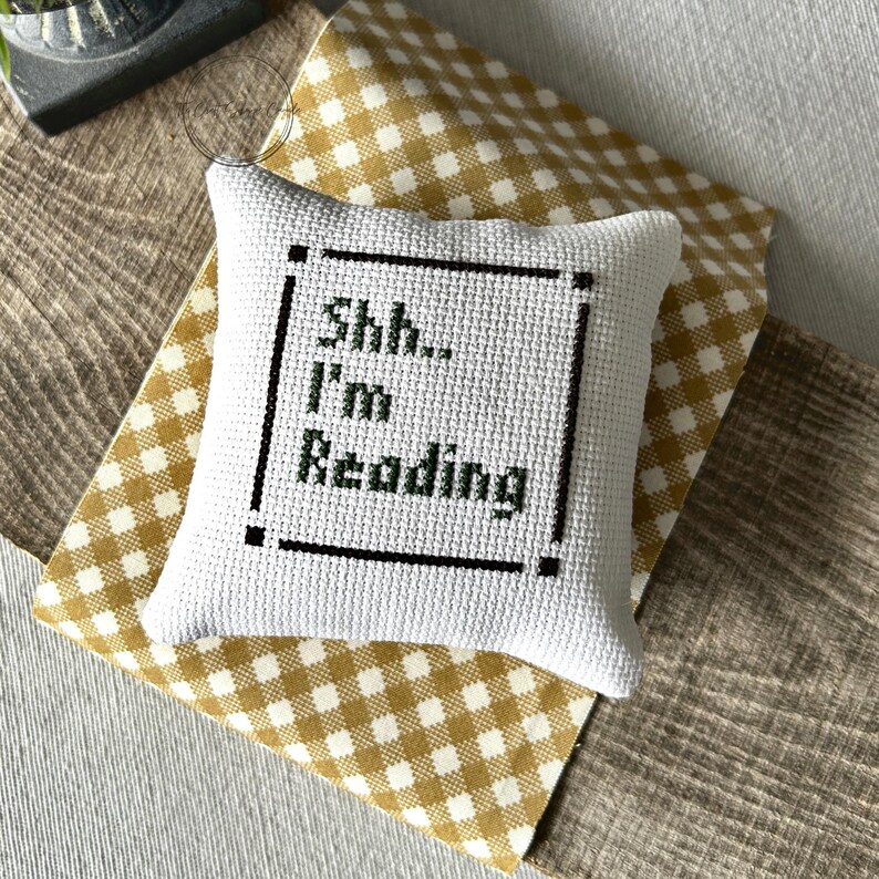 The finished pillow, made from this cross stitch pattern, is sitting on a wooden board.