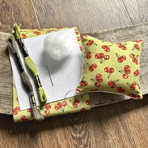 The supplies needed to make this cross stitch mini pillow are sitting on a wooden board.