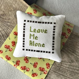 The finished pillow, made from this cross stitch pattern, is sitting on a wooden board.