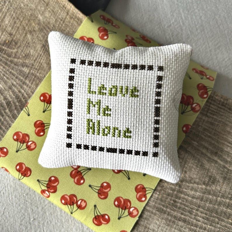 The finished pillow, made from this cross stitch pattern, is sitting on a wooden board.