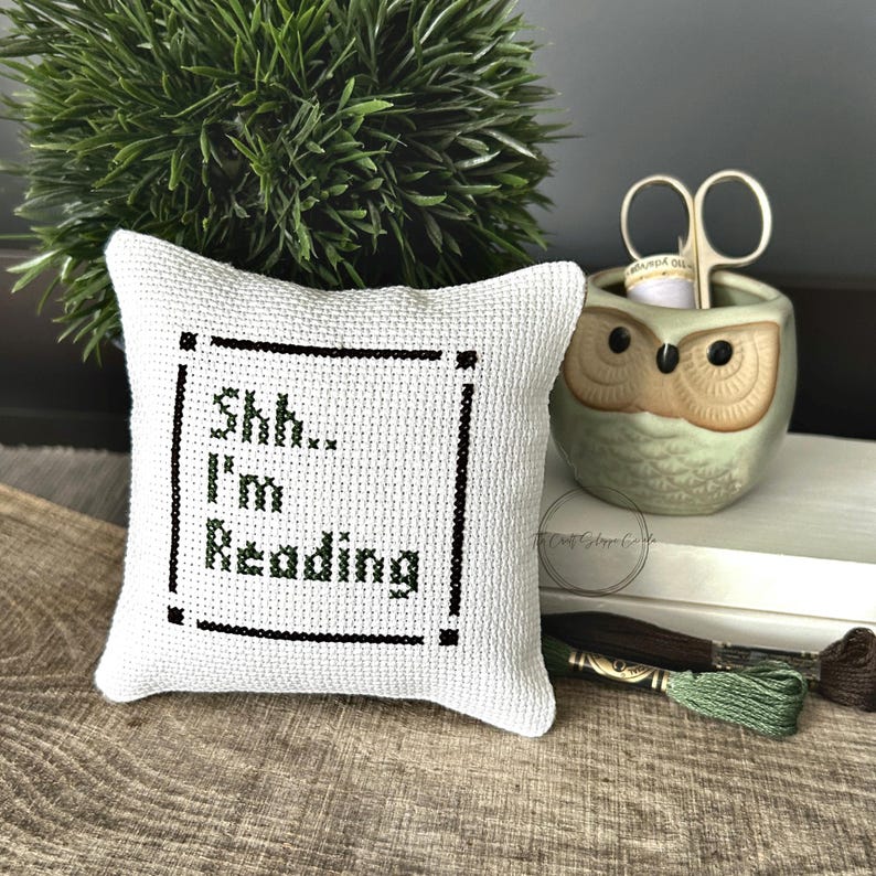 The finished pillow, made from this cross stitch pattern, is sitting on a wooden board.