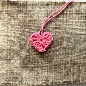 A pink heart, made from this crochet pattern, lying on a board.