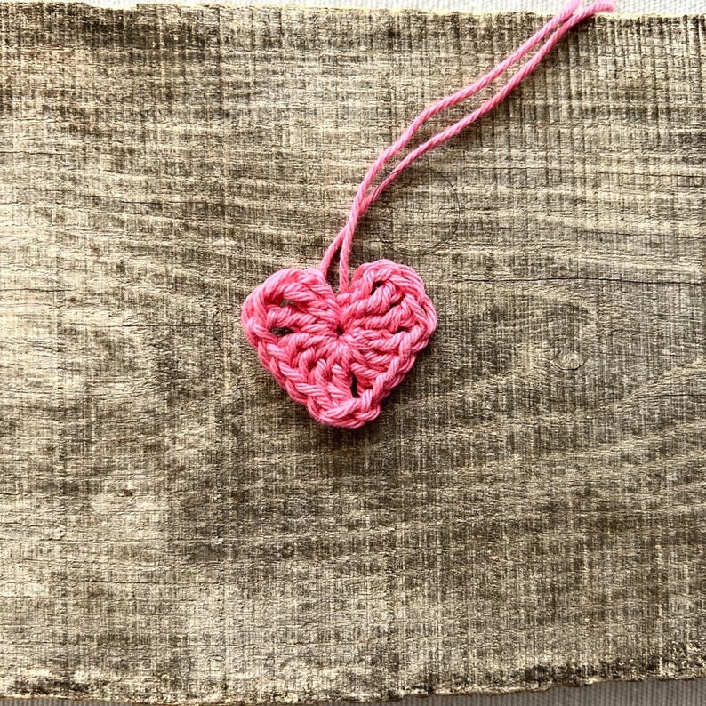 A pink heart, made from this crochet pattern, lying on a board.