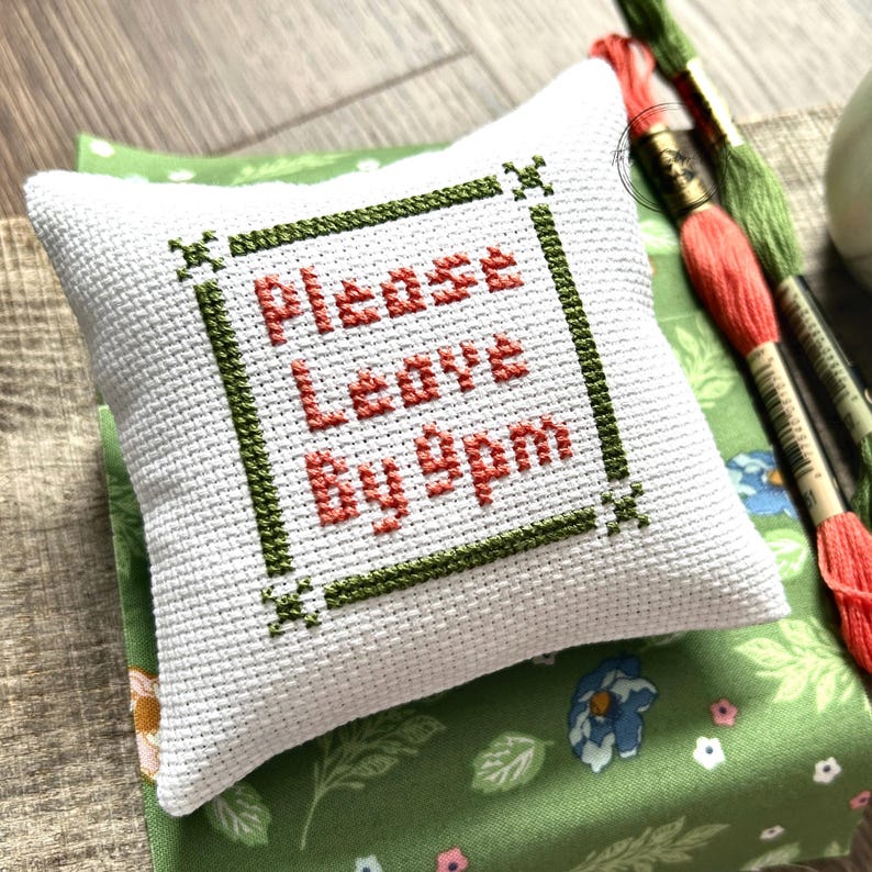 The finished pillow, made from this cross stitch kit, is sitting on a board.