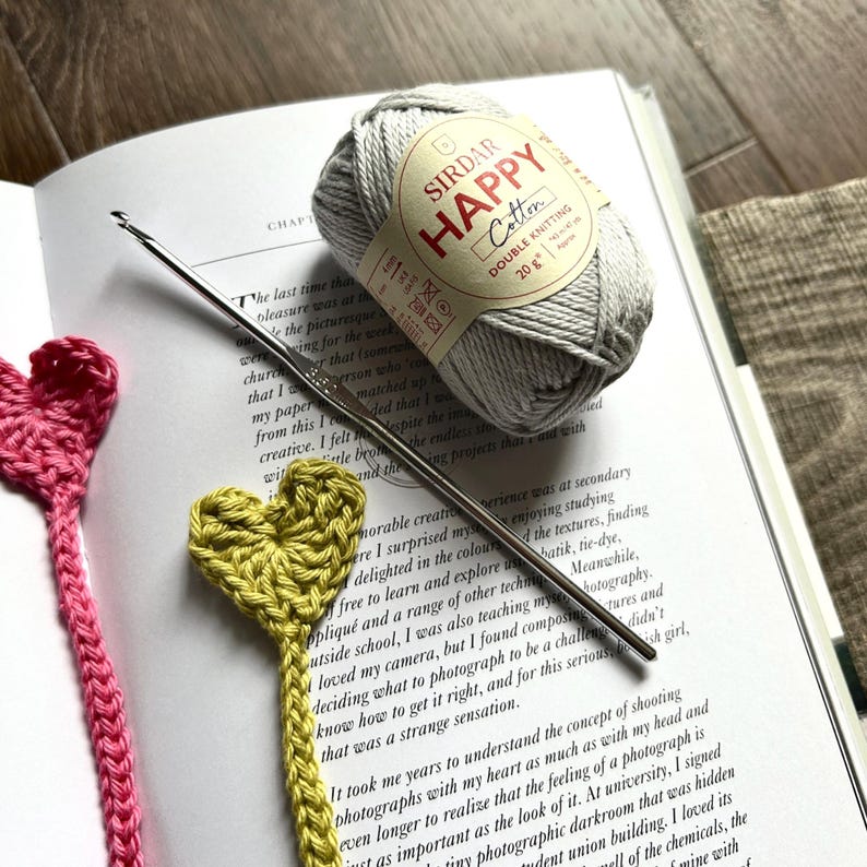 The finished bookmarks, made from this crochet pattern, are lying in a book with yarn and crochet hook.