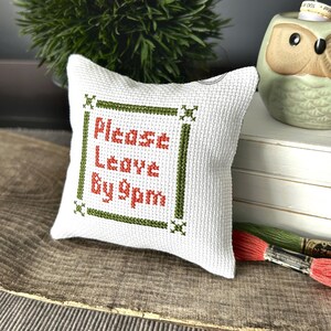 The finished pillow, made from this cross stitch pattern, is sitting on a wooden board.