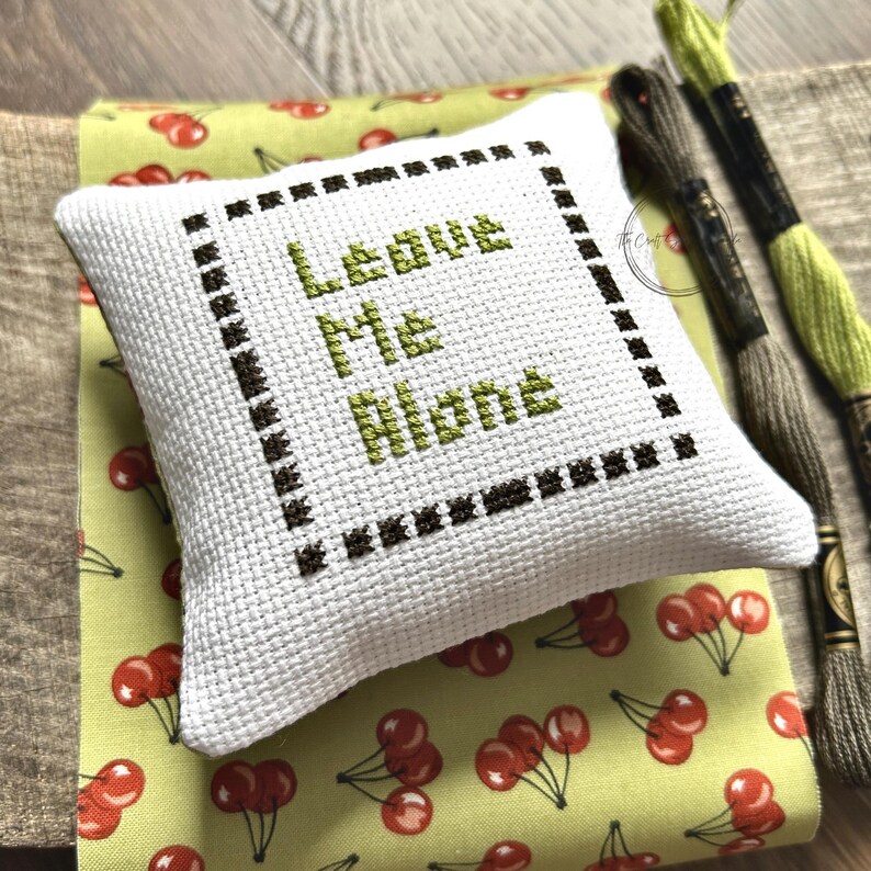 The finished pillow, made from this cross stitch pattern, is sitting on a wooden board.