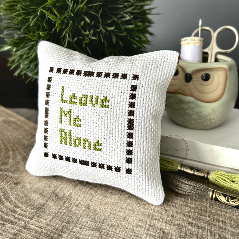 The finished pillow, made from this cross stitch pattern, is sitting on a wooden board.
