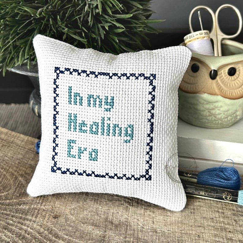 The finished pillow, made from this cross stitch pattern, is sitting on a wooden board.