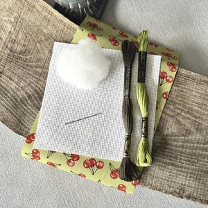 The supplies needed to make this cross stitch mini pillow are sitting on a wooden board.
