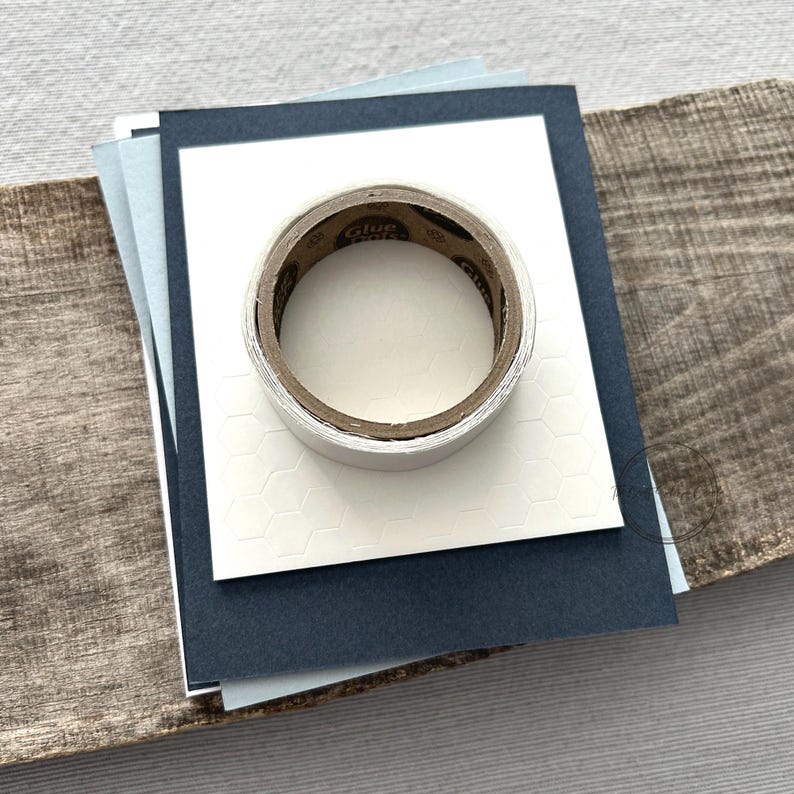 A roll of glue dots and a sheet of pop dots are sitting on a few blank cards. They are included in your card making kit.