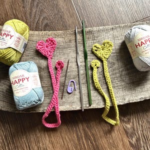 The finished bookmarks, made from this crochet pattern, are lying on a board with yarn and crochet hooks.